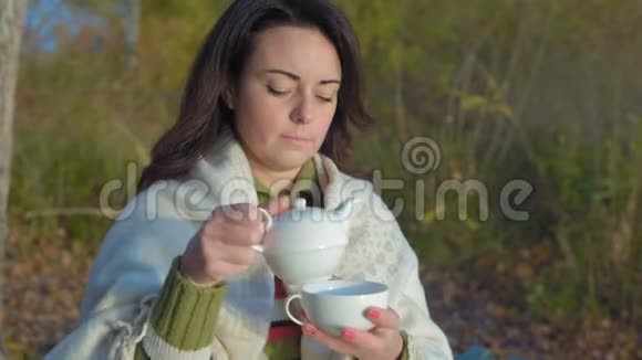 美丽的女人从瓷茶壶里倒茶茶壶里包着格子视频的预览图