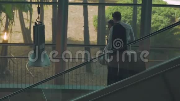 两个年轻人带着手提箱坐在自动扶梯下新婚夫妇刚度蜜月视频的预览图