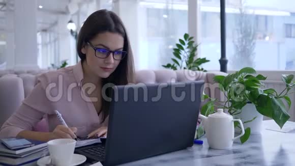 现代教育技术成功的年轻女性在工作期间在智能手机上用笔记本电脑和视频的预览图