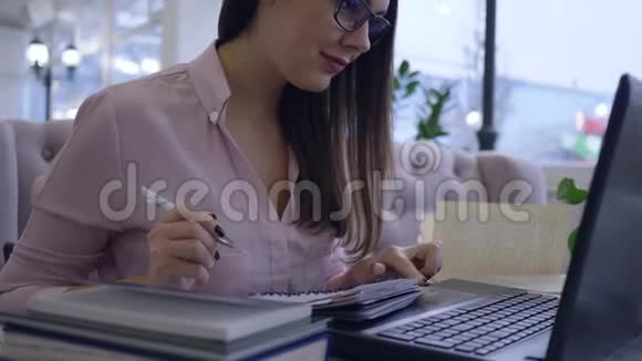 远程教育快乐的学生女孩用笔记本电脑工作用笔记本电脑做笔记坐在视频的预览图
