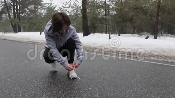 年轻漂亮的白人女孩在冬天在雪地公园跑步前系鞋带视频的预览图