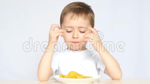 一个可爱的小男孩坐在桌子旁吃薯片对孩子来说不是健康的饮食视频的预览图
