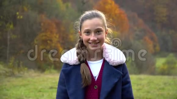 一个美丽的年轻女孩站在秋林里看着相机微笑着她高兴视频的预览图