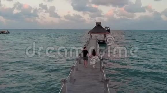 日落时分一对幸福相爱的情侣在靠近墨西哥坎昆的海滨度假胜地外的一个木码头上散步视频的预览图