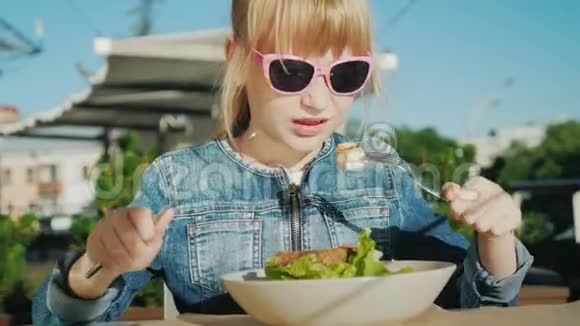 一个戴着粉红色眼镜的女孩正在一家咖啡馆的夏天操场上吃沙拉暑假与孩子的概念视频的预览图