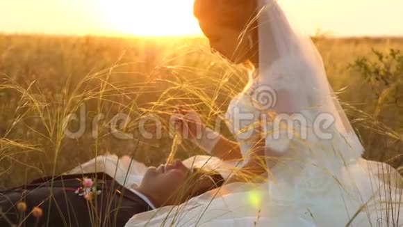 日落时分新娘和新郎正坐在田野里端着麦子互相微笑蜜月情人视频的预览图