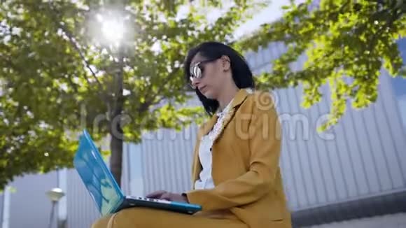 美丽的商业女性戴着太阳镜在户外休息时穿着西装使用笔记本电脑年轻女性坐着视频的预览图