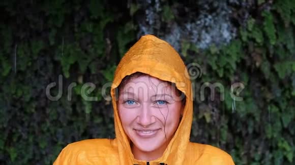 一个穿着黄色雨衣的蓝眼睛女人的肖像在镜头里看着微笑视频的预览图