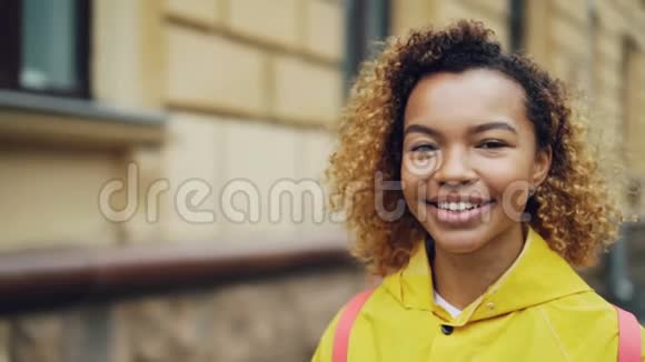 特写慢镜头可爱的混合种族年轻女士微笑着看着镜头里面有建筑物和树木视频的预览图