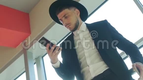 戴着帽子的白人旅行者站在车站看着电话特写慢镜头视频的预览图