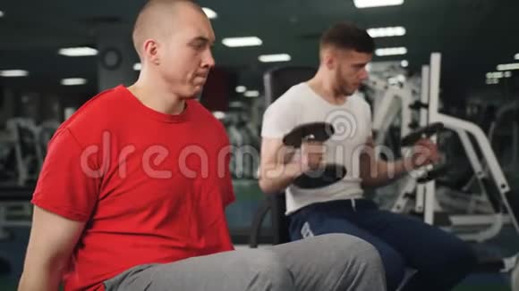两个运动健将屈臂肌肉用哑铃做运动同时坐在木托盘中视频的预览图