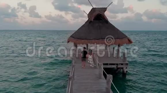 日落时分一对幸福相爱的情侣在靠近墨西哥坎昆的海滨度假胜地外的一个木码头上散步视频的预览图