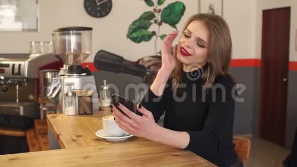 一个年轻女孩在咖啡馆的肖像手里拿着拿铁和电话视频的预览图