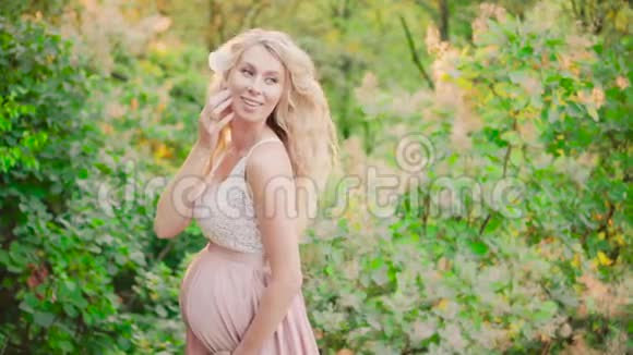 一个漂亮的怀孕少女金发碧眼在一片明亮的夏日清晨森林里在一个可爱的地方飘来飘去视频的预览图