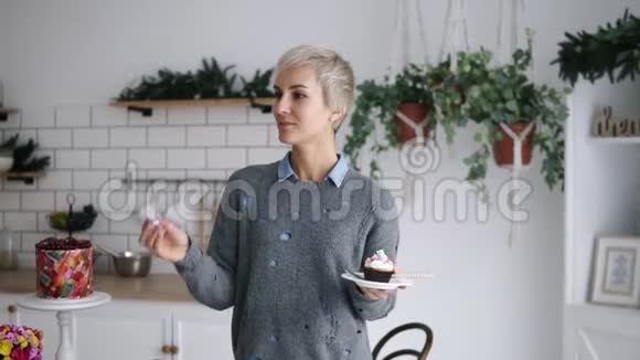 开朗快乐的女人站在厨房扔小棉花糖用嘴抓住它短灰色头发视频的预览图
