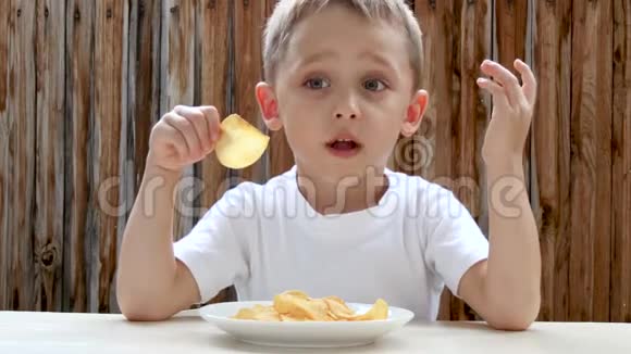 一个孩子在木墙的背景下愉快地吃薯片男孩对食物很满意视频的预览图