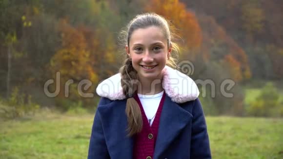 一个美丽的年轻女孩站在秋林里看着相机微笑着她高兴视频的预览图