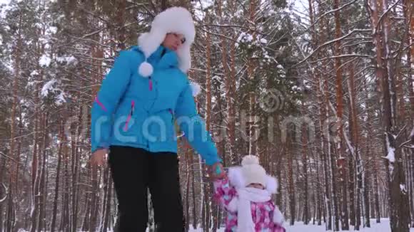 保姆在雪地路上牵着小女孩的手冬天在公园里清新的空气中散步妈妈和女儿先做视频的预览图