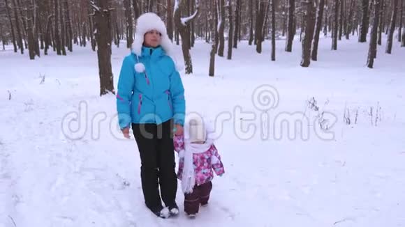 保姆在雪地路上牵着小女孩的手冬天在公园里清新的空气中散步妈妈和女儿先做视频的预览图