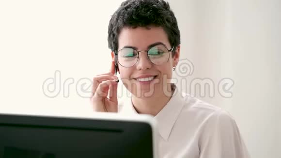 微笑的年轻商务女性使用她的自由手打电话而她的电脑在办公室工作视频的预览图