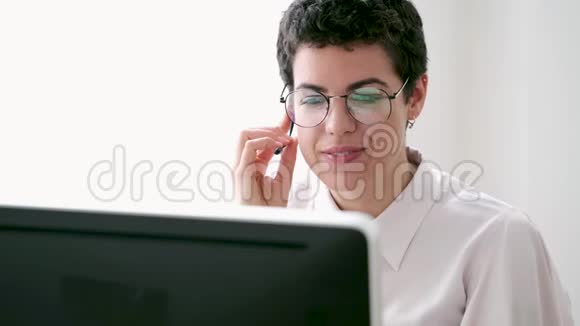 微笑的年轻商务女性使用她的自由手打电话而她的电脑在办公室工作视频的预览图