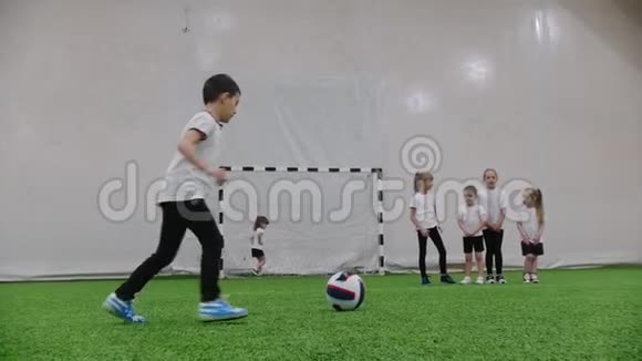 室内足球场小孩子在踢足球一个小男孩试图击中球门但女孩保护大门视频的预览图