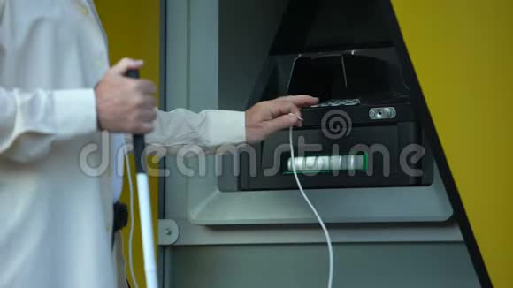 盲人在自动取款机上搜索音频插孔用耳机取钱视频的预览图
