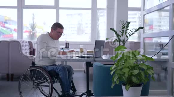 将坐在轮椅上的残疾成年男子发展成戴眼镜的人在笔记本电脑上工作视频的预览图