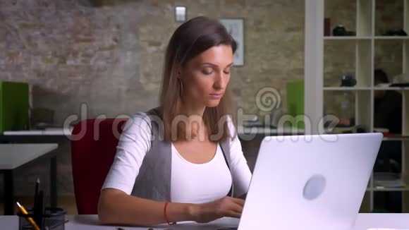 成年漂亮的女性办公室工作人员在室内工作场所专心地在白色笔记本电脑上打字视频的预览图