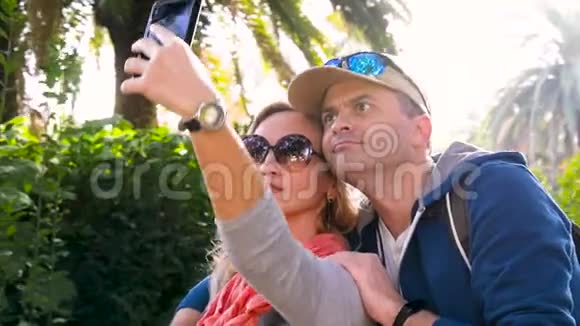 恋爱中的情侣在雨林里自拍游客在棕榈树的背景下在公园的手机上拍照视频的预览图