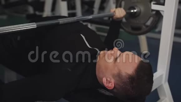年轻的健美运动员举起杠铃躺在健身房里的一个女仆身上在教练的控制下男人可以提高自由体重视频的预览图