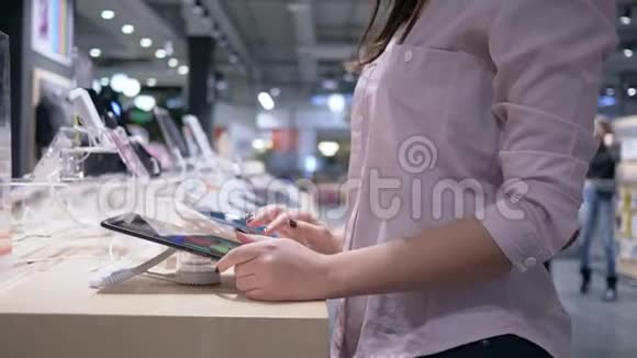 在电子商店购物美丽的女孩使用最新的现代平板电脑并考虑购买视频的预览图