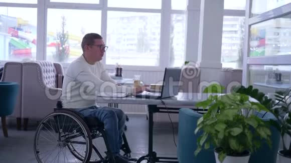 在线支付快乐残疾人戴着塑料卡坐在轮椅上的眼镜使用现代互联网购买视频的预览图