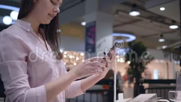 电子商店迷人的女孩买家选择和测试现代手机附近的橱窗视频的预览图