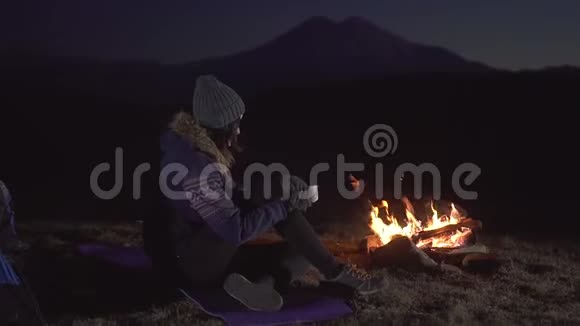 夜深人静的时候一个年轻的女人坐着喝着杯酒在山上的炉火旁慢慢地视频的预览图