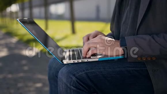 快关门男性手在电脑键盘上打字户外年轻的商人坐在长凳上用笔记本电脑男子视频的预览图