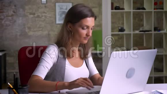 漂亮的女办公室职员坐在笔记本电脑前把视线转向相机满意地微笑着视频的预览图