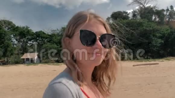 年轻的欧洲女孩戴着太阳镜在沙滩上海涛的背景下散步视频的预览图