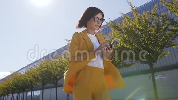 戴墨镜的年轻女商人在城市街头散步在外面使用现代智能手机的肖像视频的预览图