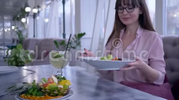 咖啡馆里的营养很好年轻女子戴着眼镜手里拿着叉子和盘子吃着希腊色拉看上去很漂亮视频的预览图