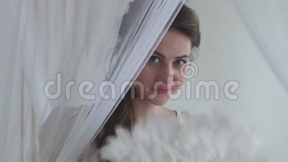 肖像可爱的女人挥舞白色羽毛扇子在白色背景真人系列躲在面纱后面视频的预览图