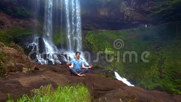 集中注意力的人在瀑布的瑜伽垫上冥想视频的预览图