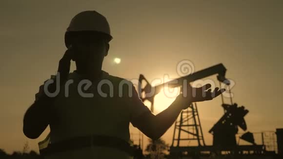人力工程师剪影带电话监督日落时原油生产现场视频的预览图