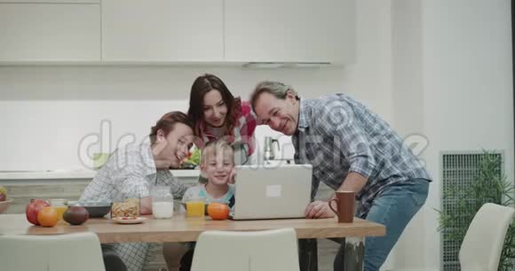在现代厨房设计中一个成熟的家庭在早上观看笔记本电脑的视频同时拍摄健康的家庭视频的预览图