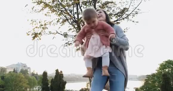 在公园日落时漂亮的年轻女子抱着小女孩快乐的妈妈玩耍拥抱和亲吻她的小女儿视频的预览图