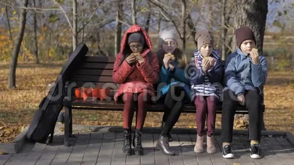 一群饥饿的孩子在阳光明媚的秋日在公园户外吃汉堡视频的预览图