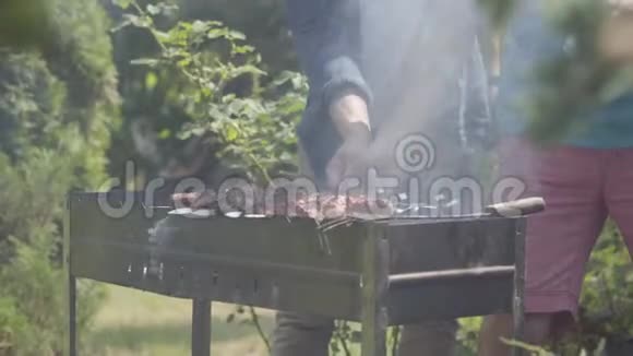 无法辨认的男人在花园里做烧烤夏日休闲朋友们在烤架上煮肉视频的预览图