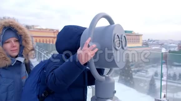 在冬天妈妈和儿子通过望远镜在城市的屋顶上看视频的预览图