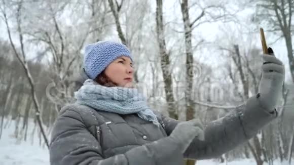 在冬季公园微笑的成年女人在电话里自拍视频的预览图