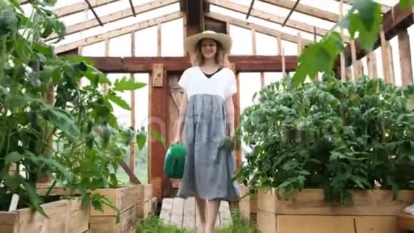 戴着草帽和裙子的女人拿着浇水罐去温室视频的预览图